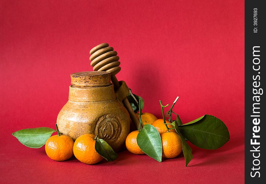 Still life of a hone pot with dipper and tangerines with leaves on red background illuminated by the morning sun from the side. Still life of a hone pot with dipper and tangerines with leaves on red background illuminated by the morning sun from the side