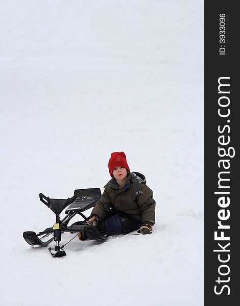 A young boy enjoying a winter day resting at the bottom of a steep toboggan hill with his sled