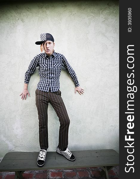 Teenage boy standing on a green bench in front of a stucco wall. Teenage boy standing on a green bench in front of a stucco wall