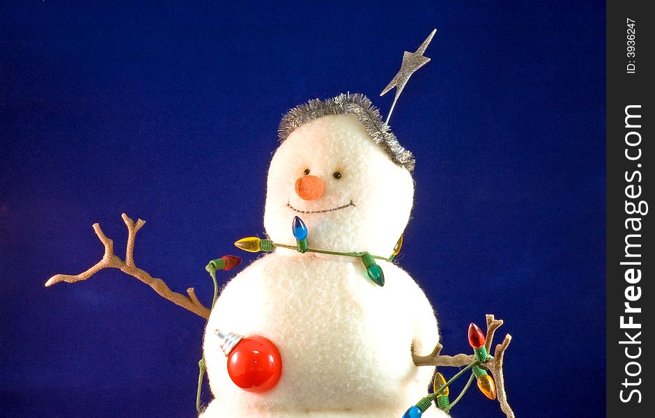 A colorfully stuffed toy snowman wearing Christmas decorations, isolated on a blue background. A colorfully stuffed toy snowman wearing Christmas decorations, isolated on a blue background.