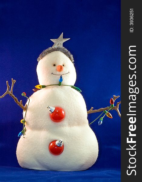 A colorfully stuffed toy snowman with stick arms and wearing Christmas decorations, isolated on a blue background. A colorfully stuffed toy snowman with stick arms and wearing Christmas decorations, isolated on a blue background.