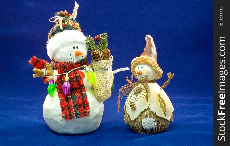 Two colorfully toy snowmen wearing Christmas decorations, isolated on a blue background. Two colorfully toy snowmen wearing Christmas decorations, isolated on a blue background.