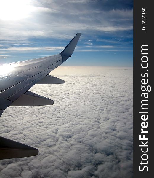 View from aircraft window showing wing and clouds below. View from aircraft window showing wing and clouds below