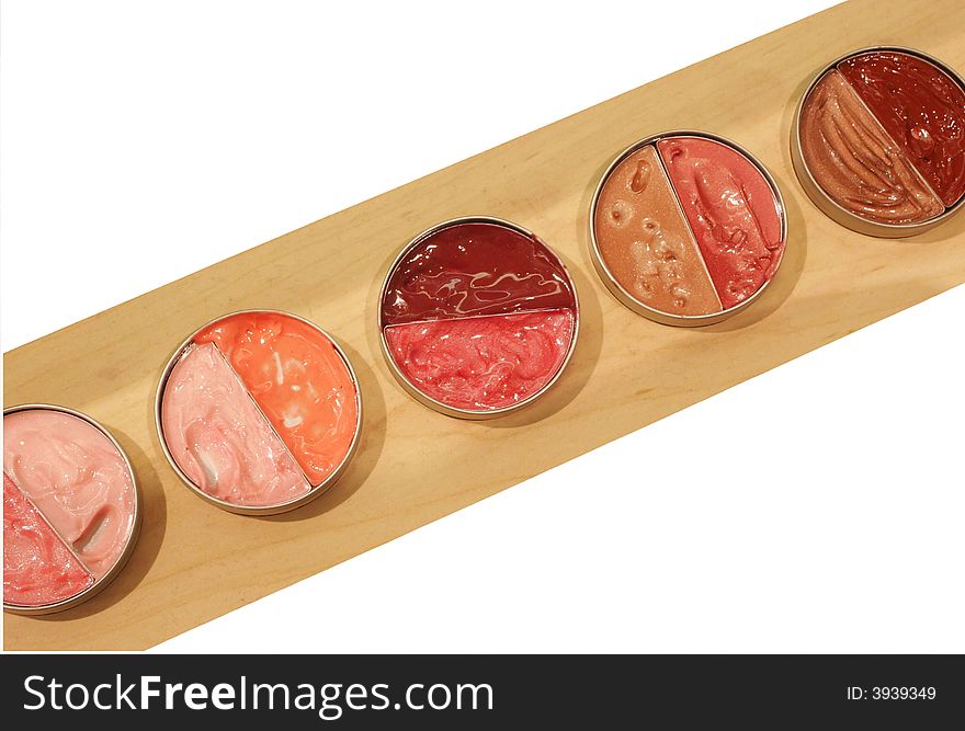Row of colorful pots of lip gloss displayed on wood shelf and isolated on white background. Row of colorful pots of lip gloss displayed on wood shelf and isolated on white background.