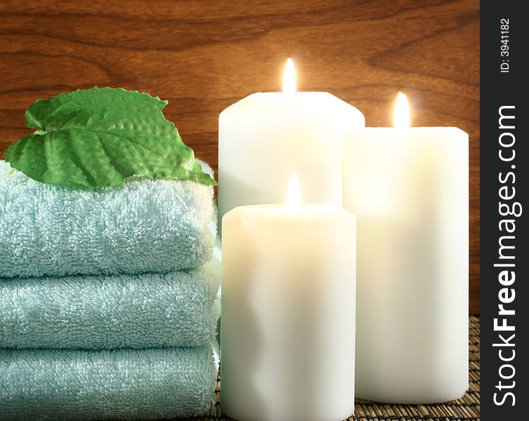 Blue towel, white candle, green leaf in front of wood background. Blue towel, white candle, green leaf in front of wood background