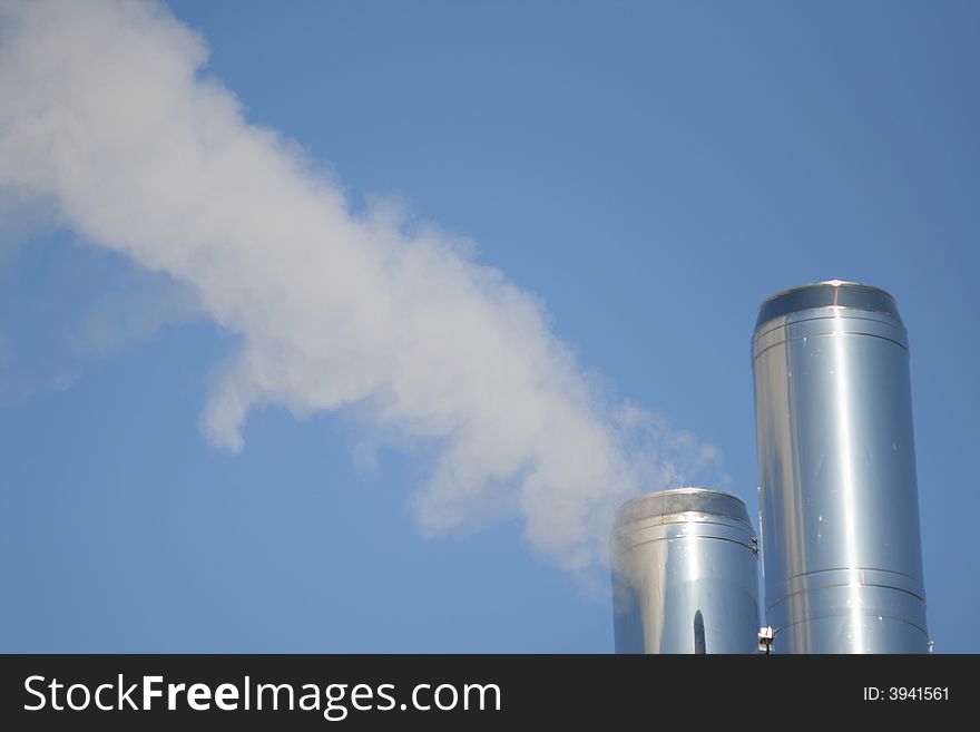 Two chimneys with a smoke on a background of the blue sky