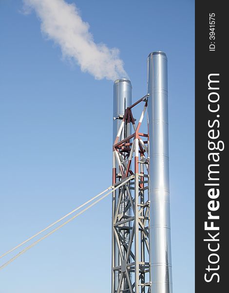 Two chimneys on a metal farm with a smoke on a background of the blue sky