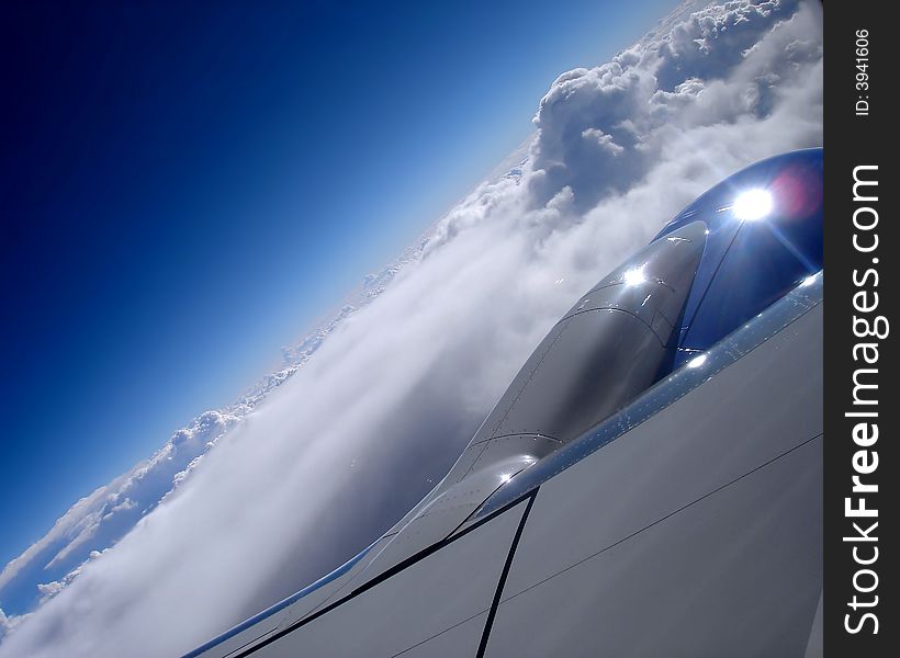 Photo of an airplane engine taken from inside the plane while flying above blue skies and fluffy white clouds. Photo of an airplane engine taken from inside the plane while flying above blue skies and fluffy white clouds.