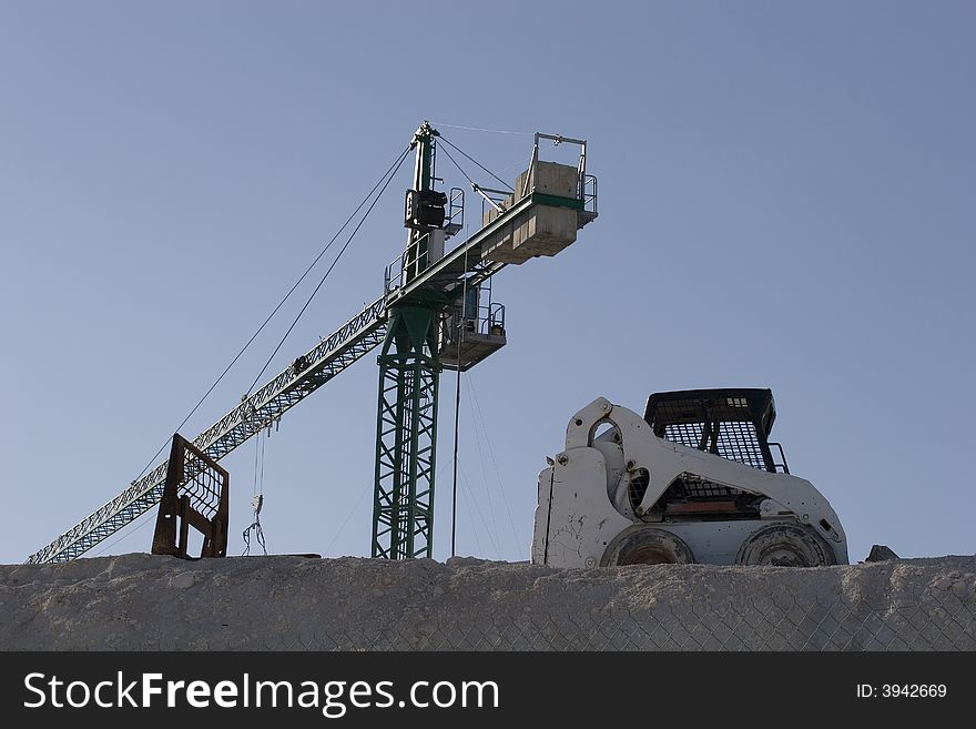 A construction site against blue sky with a crane and a small bulldozer. A construction site against blue sky with a crane and a small bulldozer