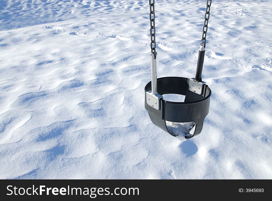 A lonely swing over the snow in a playground.