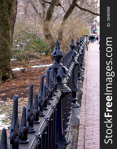 Ornate wrought iron fence running along brick sidewalk on a winter day