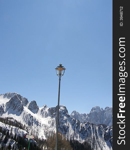 Vintage lamp in mountain village, beautiful mountain peaks and alpine vegetation covered in snow, clear blue sky winter day