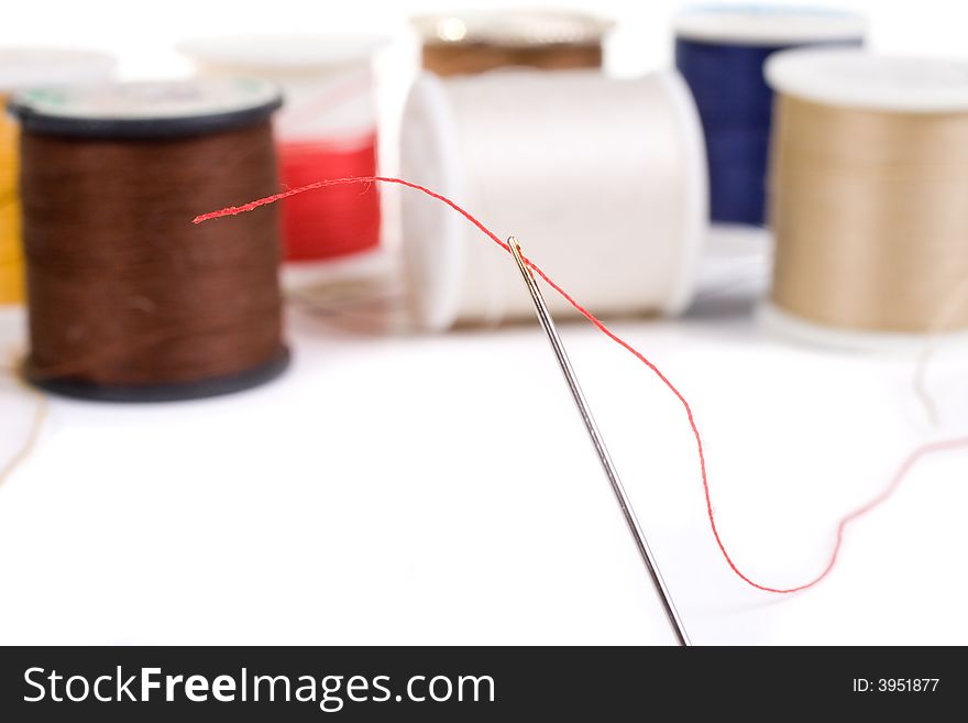 Sewing needle threaded with red, various colored spools in background. Sewing needle threaded with red, various colored spools in background