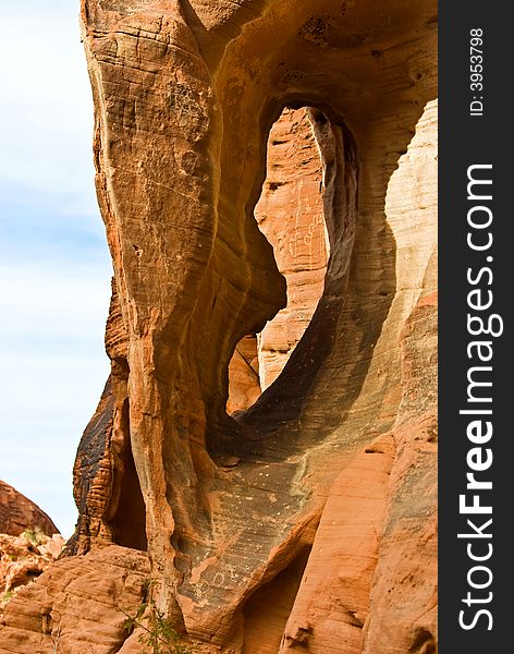 Rock formation with arch and Native American petroglyphs on canyon wall in background - Valley of fire SP