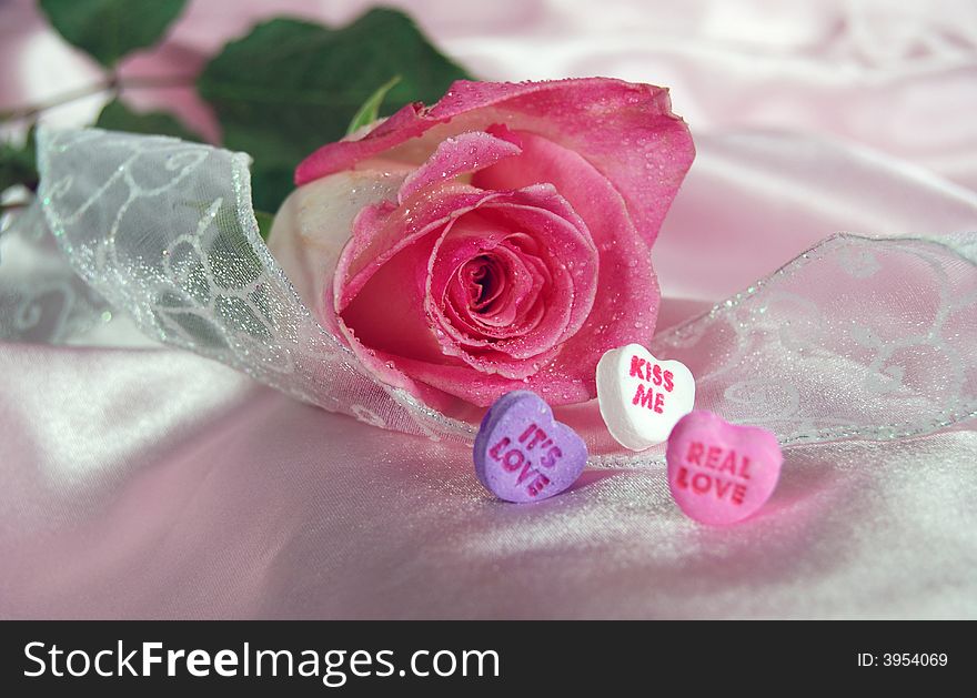Single pink rose with sparkling ribbon and candy hearts on satin. Single pink rose with sparkling ribbon and candy hearts on satin.