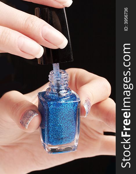 Woman applying blue glittering nailpolish, party manicure , black background
