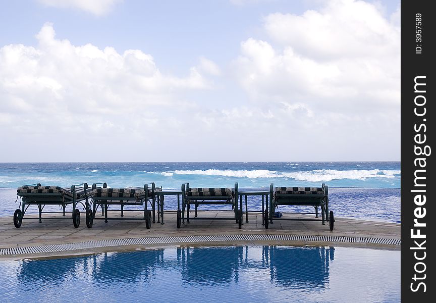 Four chaise lounges on a deck between the pool and the ocean. Four chaise lounges on a deck between the pool and the ocean