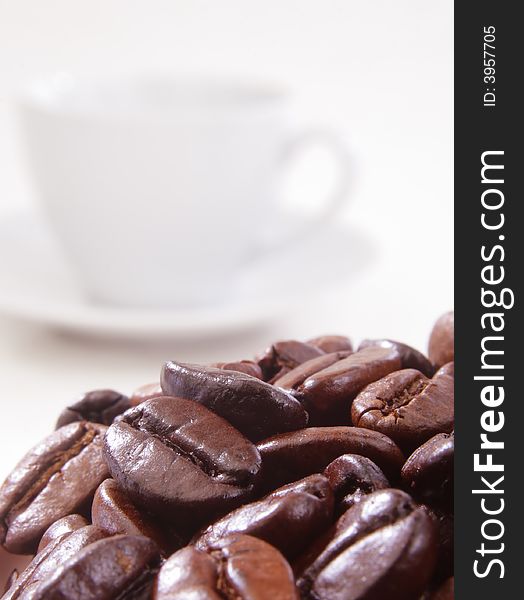 Close up of coffee beans with a cup in background. Close up of coffee beans with a cup in background.