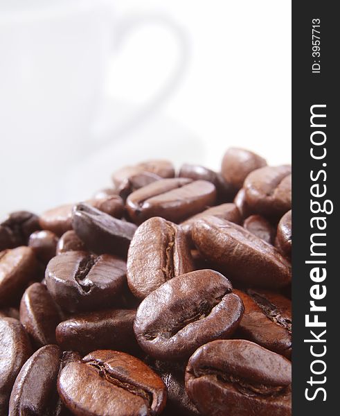 Close up of coffee beans with a white cup in background. Close up of coffee beans with a white cup in background.