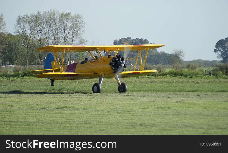 Yellow vintage biplane taking off a field