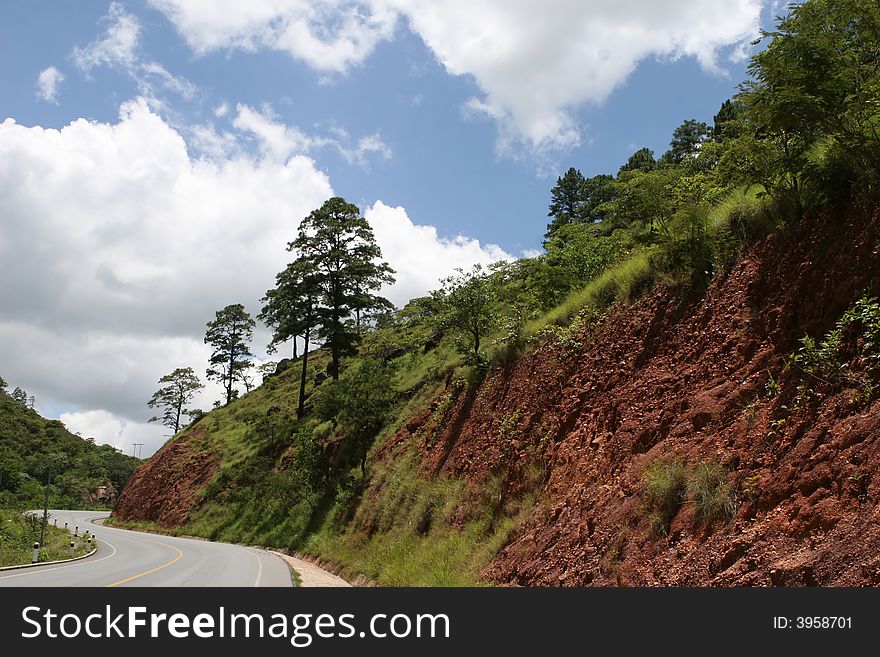 A curved road leads around a large mountain embankment. A curved road leads around a large mountain embankment