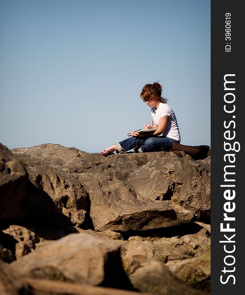 Young woman sketching while sitting high on a pile of boulders. Young woman sketching while sitting high on a pile of boulders.