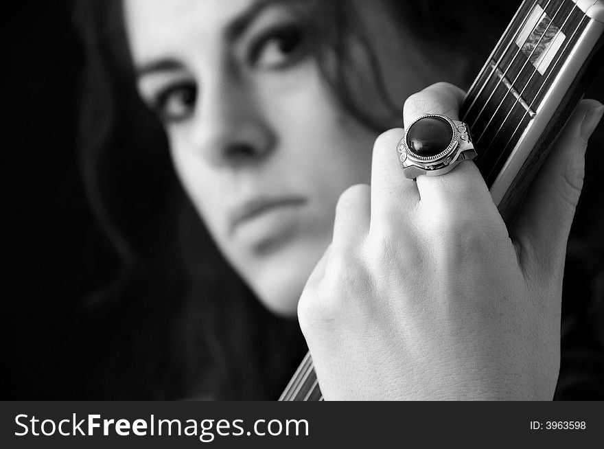 Beautiful brunette on black background playing guitar