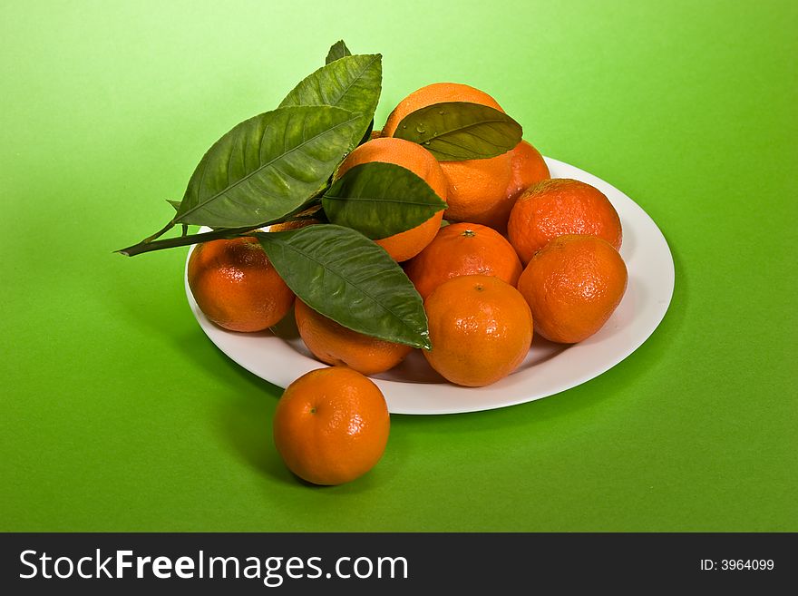 Several ripe tangerines on the plete over green background