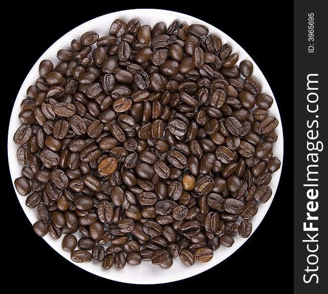 Coffee beans on white plate isolated against black background