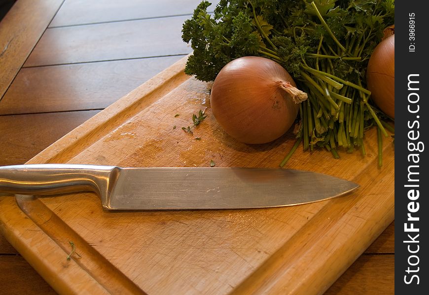 A cutting board with an onion and herbs ready to be cut.