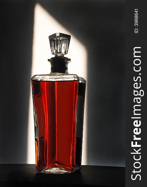A brandy bottle stands backlit, displaying the saturated color of itâ€™s contents. A brandy bottle stands backlit, displaying the saturated color of itâ€™s contents.