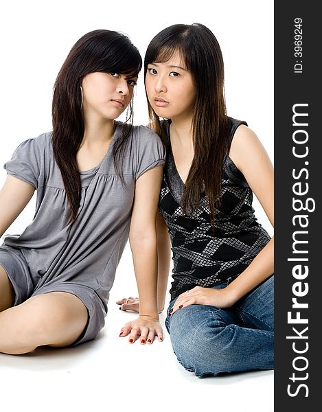 Two young Asian women sitting together on white background. Two young Asian women sitting together on white background