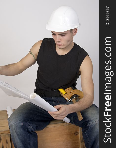 Young man in hard hat and toolbelt studying a set of blueprints. Young man in hard hat and toolbelt studying a set of blueprints.
