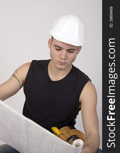 Young man wearing hardhat and toolbelt studying set of blueprints. Young man wearing hardhat and toolbelt studying set of blueprints.