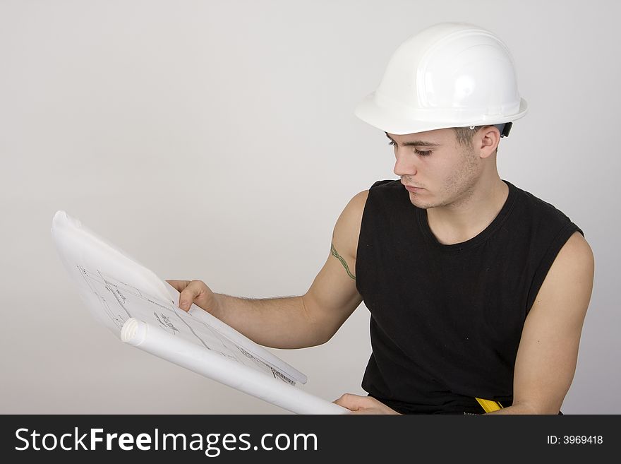Young man in hardhat looking over a set of blueprints. Young man in hardhat looking over a set of blueprints