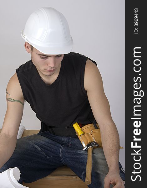 Young man in a hardhat land toolbelt ooking at blueprints. Young man in a hardhat land toolbelt ooking at blueprints