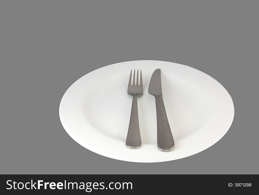 Knife and fork on a plate isolated against a grey background. Knife and fork on a plate isolated against a grey background