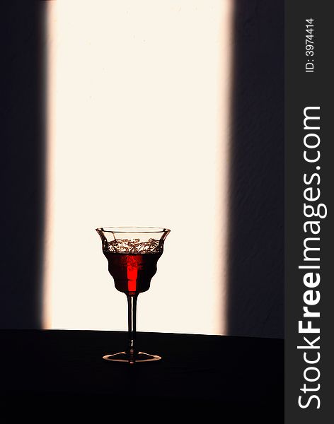 A solitary glass of wine stands beautifully backlit to show the rich color of it’s contents. A solitary glass of wine stands beautifully backlit to show the rich color of it’s contents.