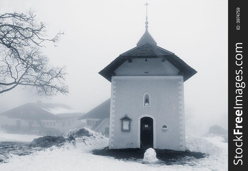 A small church surrounded by snow, with a half-melted snowman in front of the entrance. A small church surrounded by snow, with a half-melted snowman in front of the entrance.