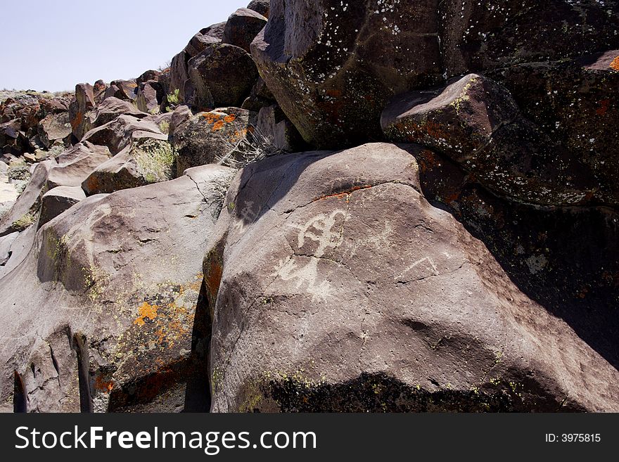 Native American rock art petroglyphs of anthropomorphic like figures shooting arrows carved into desert varnish and lichen covered boulders in Little Petroglyph Canyon of the Coso Range in California. Native American rock art petroglyphs of anthropomorphic like figures shooting arrows carved into desert varnish and lichen covered boulders in Little Petroglyph Canyon of the Coso Range in California