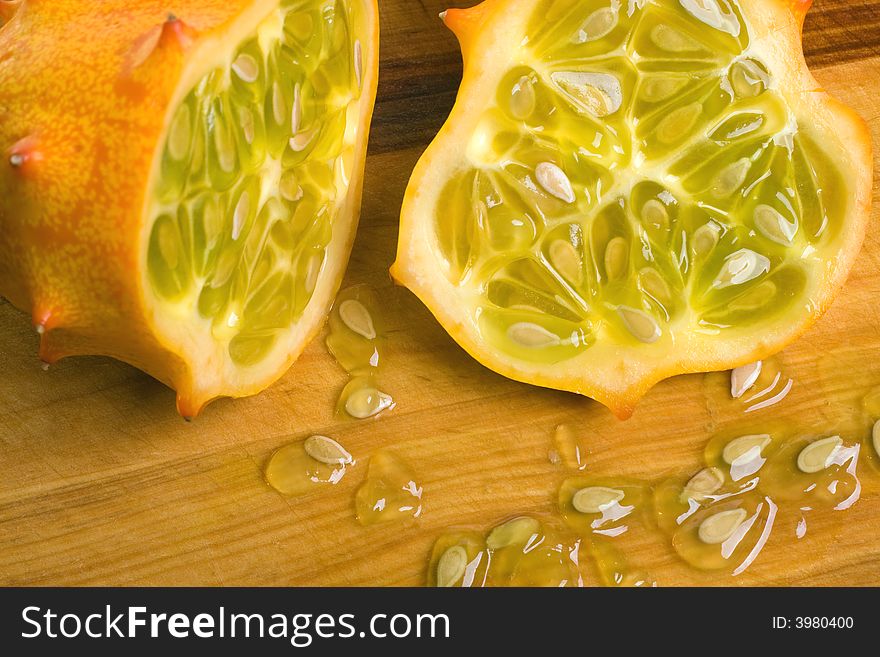 A juicy sliced open horned or Kiwano melon showing the seeds and yellow-green flesh on cutting board. A juicy sliced open horned or Kiwano melon showing the seeds and yellow-green flesh on cutting board