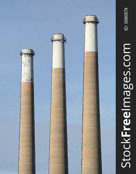 Three large industrial smokestacks against a pale blue sky. Three large industrial smokestacks against a pale blue sky