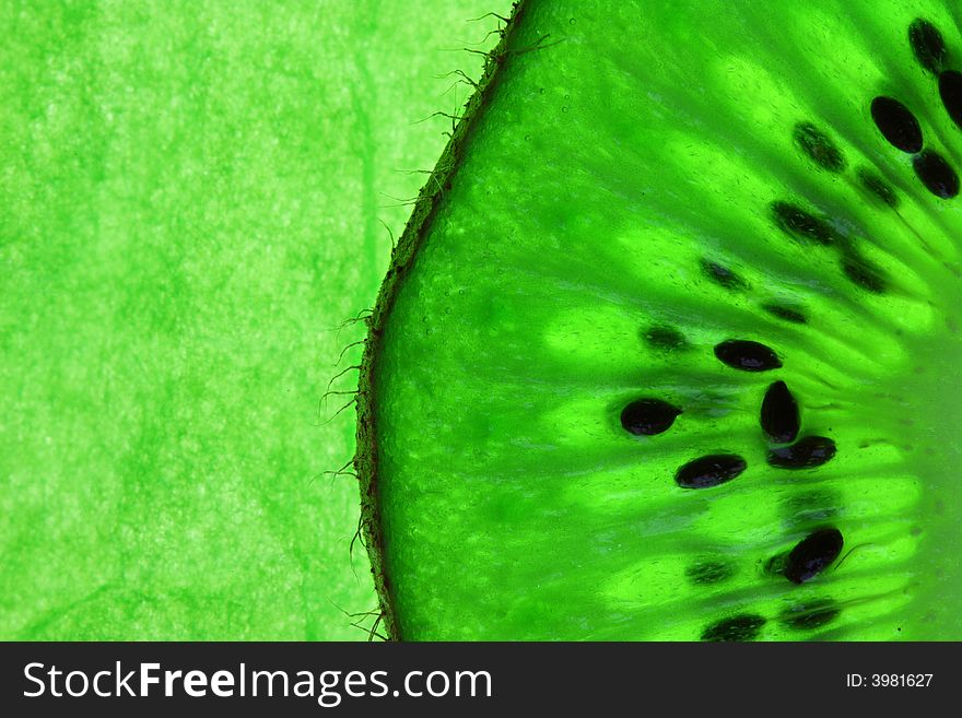 Slice of kiwi fruit on rough  green background, back light, close-up. Slice of kiwi fruit on rough  green background, back light, close-up