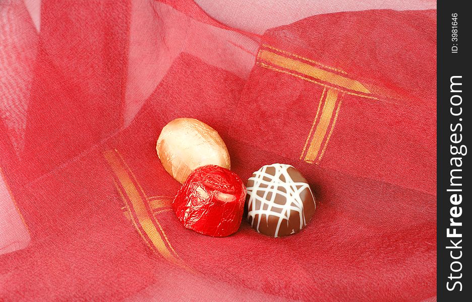 Three fancy chocolates on a piece of red fabric.