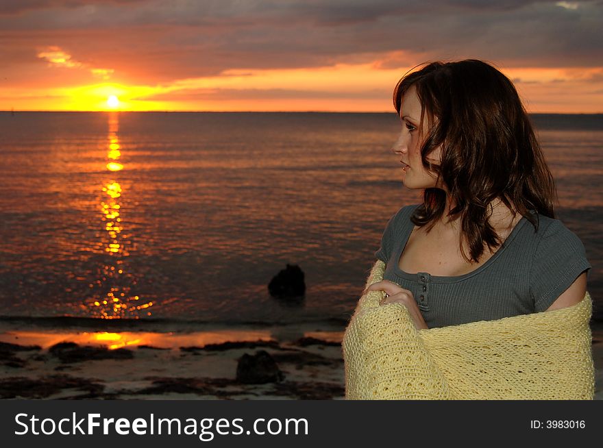 Young woman wrapped in a blanket at the beach looking out to the sunset. Young woman wrapped in a blanket at the beach looking out to the sunset.