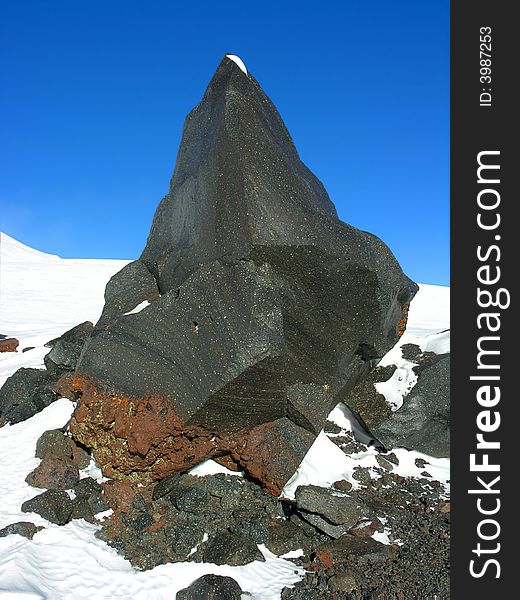 Fragment of a black rock on a snow on a background of the blue sky