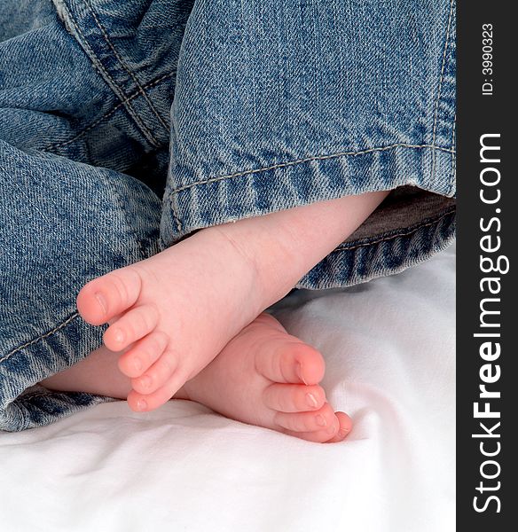 Feet of baby in blue jeans on white blanket. Feet of baby in blue jeans on white blanket