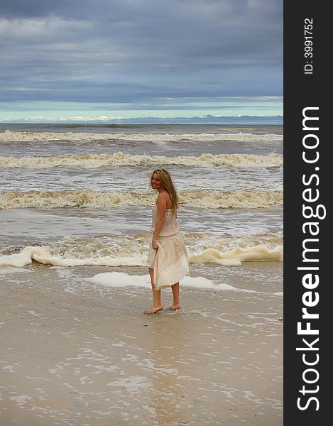 Beautiful girl at the stormy beach walking in the water