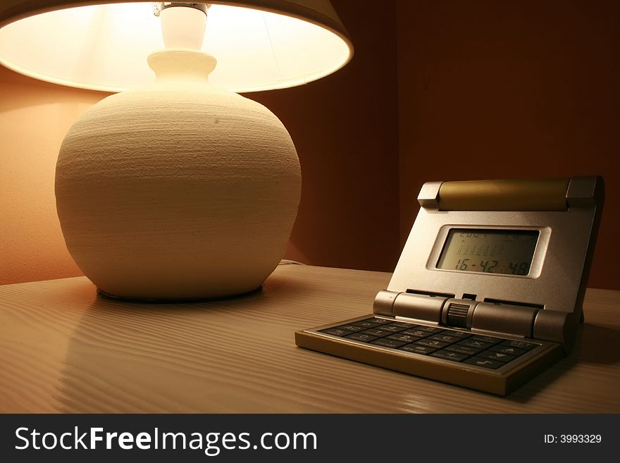 Stone lamp and travel clock on a wooden cabinet in a dark interior of a hotel room. Stone lamp and travel clock on a wooden cabinet in a dark interior of a hotel room