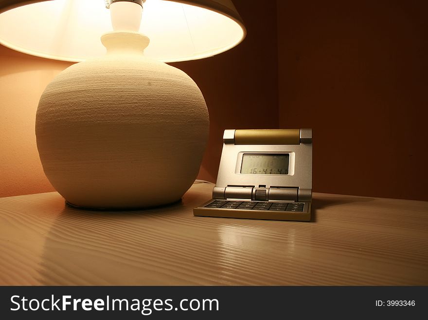 Stone lamp and travel clock on a wooden cabinet in a dark interior of a hotel room. Stone lamp and travel clock on a wooden cabinet in a dark interior of a hotel room